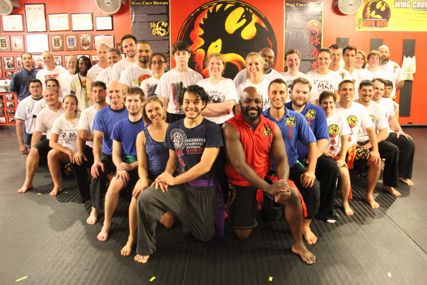 group shot of wing chun martial arts students posing in front of sifu och wing chun logo